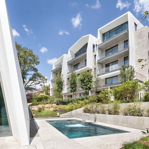 Moderne, zweigeschossige Luxus-Wohnblöcke mit Balkonen und einem Pool mit viel grün drumherum zwischen den Wohnblöcken im Sonnenlicht
