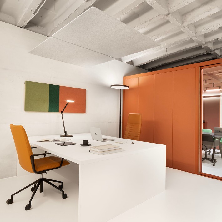 Modernes, minimalistisches Büro mit zwei gegenüberstehenden Schreibtischen, Schreibtischstühle und ein großer Aktenschrank in orange und schwarzen Deisgnerlampen, ein macbook steht auf einem Schreibtisch