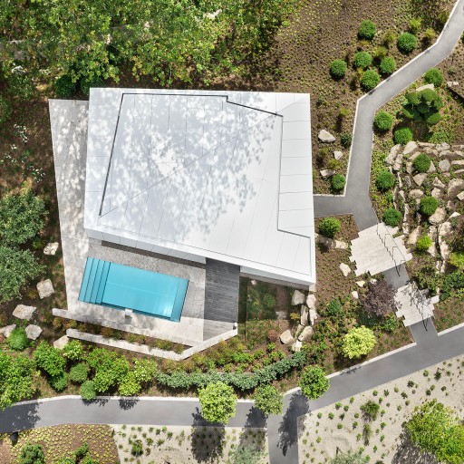 Luftaufnahme mit Blick senkrecht auf einen futuristischen weißen Bungalow in einer mordernen Gatrneanlage mit rechteckigigem Pool