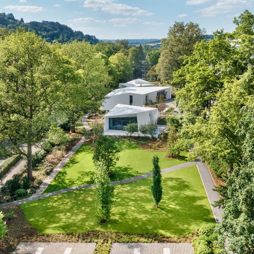 Futuristische weiße Bungalows in einem klar strukturierten Garten umgeben von hohen Bäumen