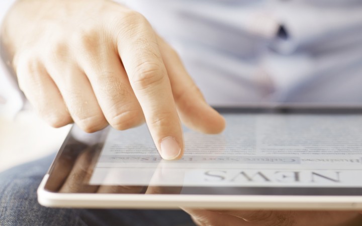 Männliche Hand scrollt auf einem Tablet, auf dem man erkennenkann, dass es sich um eine News-Seite handelt.