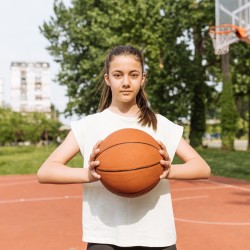 Mädchen hält einen Basketball in der Hand und blickt in die Kamera