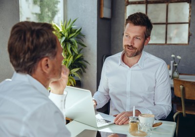 Zwei Männer in weißen Hemden sitzen sich während eines Beratungsgesprächs an einem Schreibtisch gegenüber