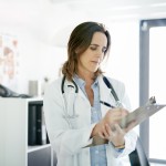 Ärztin steht in einem beratungszimmer und schreibt auf ein Klemmbrett