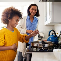 Pre-teen Mädchen steht am Herd in der Küche mit Spachtel und Pfanne, Zubereitung von Speisen mit ihrer Mutter, seitliche Ansich