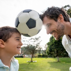 Vater und Sohn halten einen Fußball zwischen ihren Köpfen