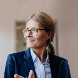 Blonde Businessfrau mit Zopf und Brille im Hosenanzug schaut lächelnd nach links