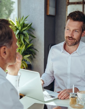 Zwei Männer in weißen Hemden sitzen sich während eines Beratungsgesprächs an einem Schreibtisch gegenüber