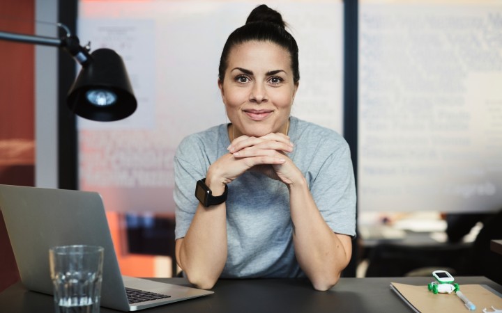 Frau sitzt am Schreibtisch und stützt ihr Kinn entspannt auf ihre verschränkten Hände