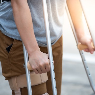 Mann geht mit zwei Krücken und einer Beinschiene