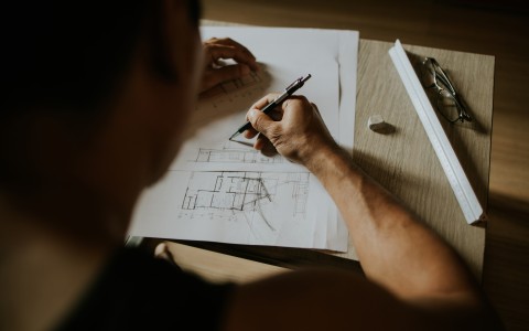 Mann am Schreibtisch zeichnet einen Grundriss