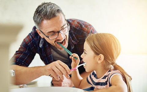 Ein Mann und seine kleine Tochter putzen zusammen die Zähne