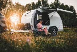 Wohnwagen mit Frau, die vor dem Wohnwagen sitzt