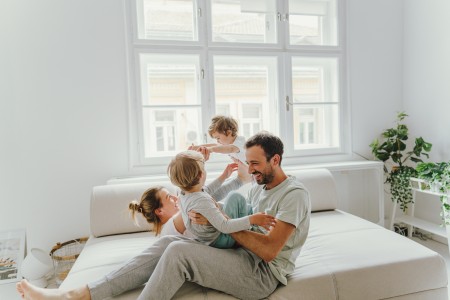 Familie tobt glüklich auf dem Sofa in einm hellen Wohzimmer