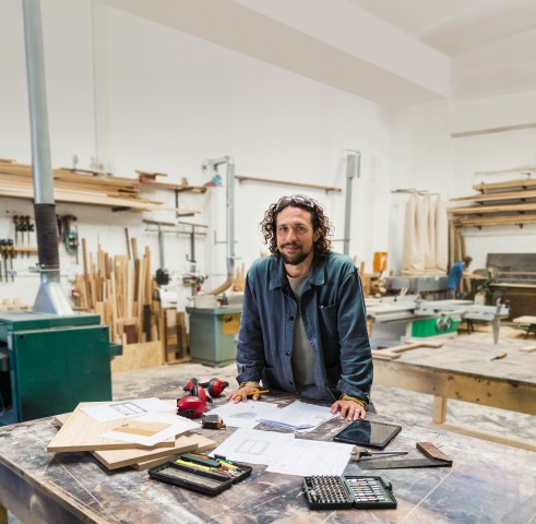Mann in einer Werkstatt an einem Tisch mit Unterlagen und Werkzeugen